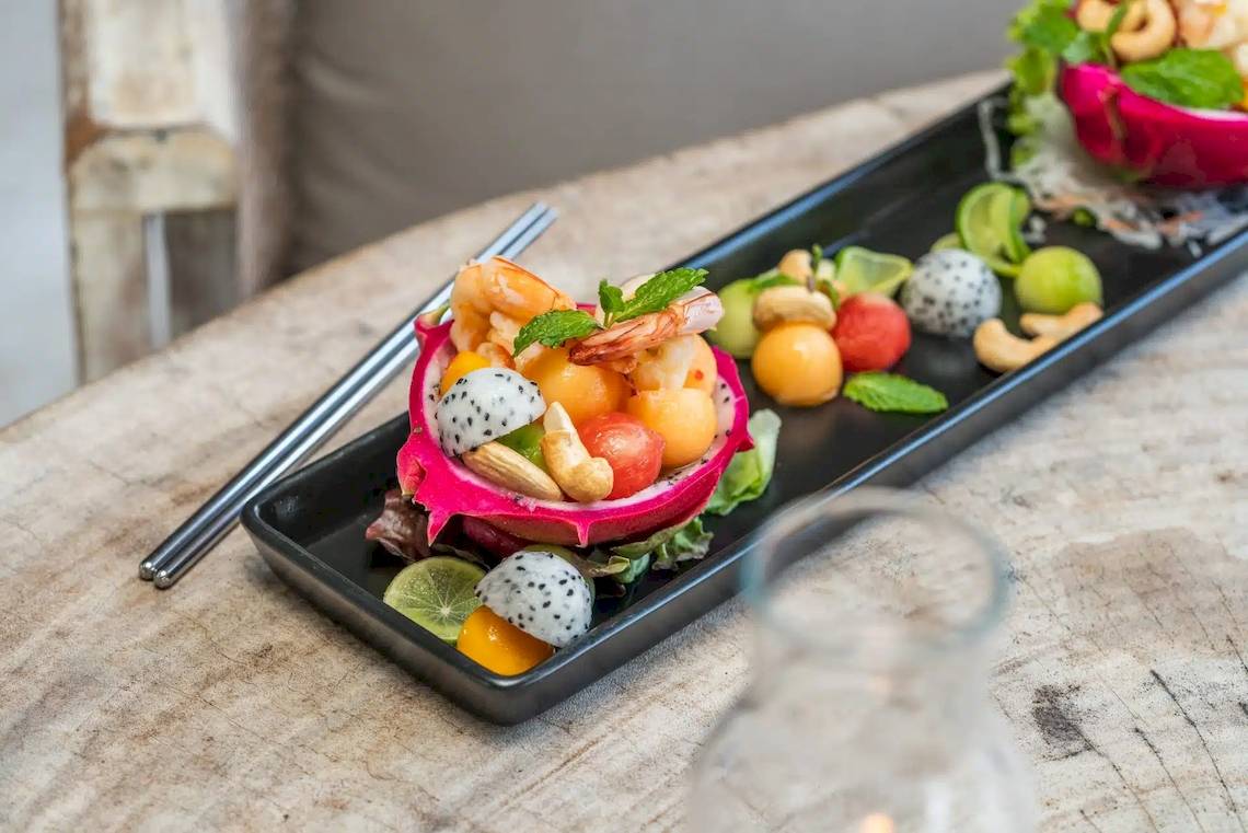 Ein schwarzer Teller mit einem bunten Fruchtsalat, serviert auf einem Holztisch.