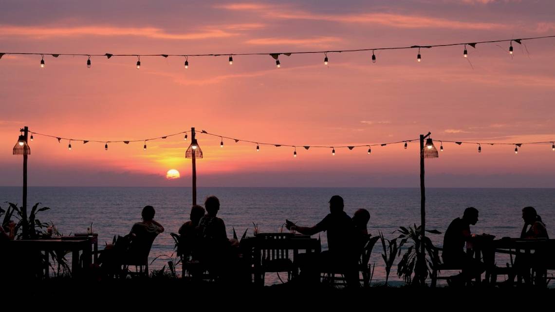 Menschen sitzen bei Sonnenuntergang am Meer auf einem Tisch im Freien des Haadson Resorts.