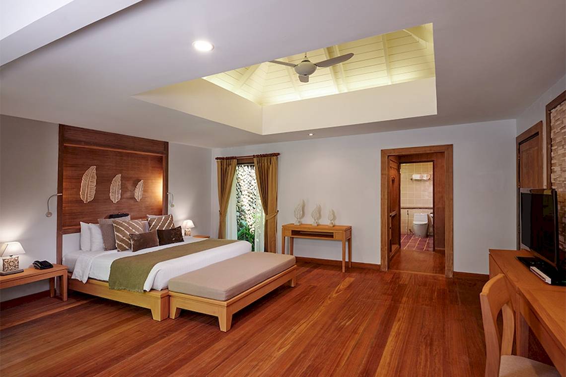 Innenansicht eines Zimmers im Khaolak Paradise Resort mit großem Bett, Holzboden und Glasfenstern.