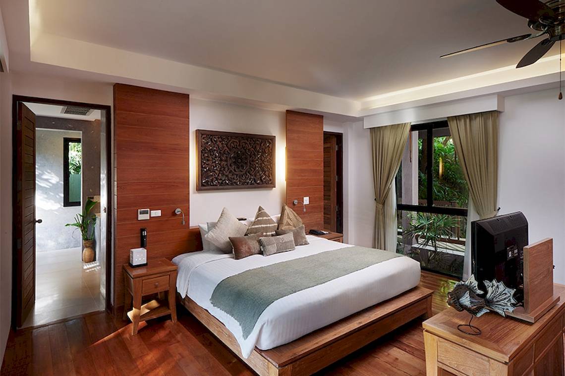 Innenansicht eines Schlafzimmers im Khaolak Paradise Resort mit großem Bett, Holzmöbeln und einem Fernseher auf einem Nachttisch.