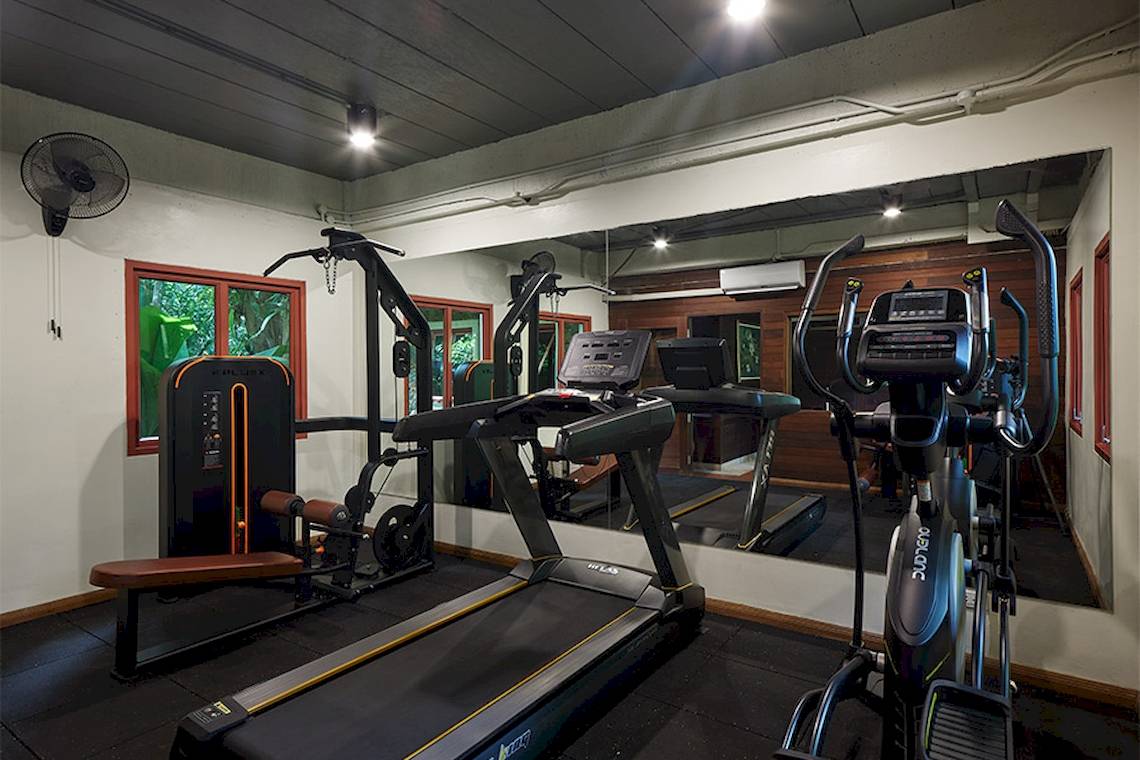 Fitnessraum im Khaolak Paradise Resort mit Laufband, Hanteln und einem großen Spiegel.