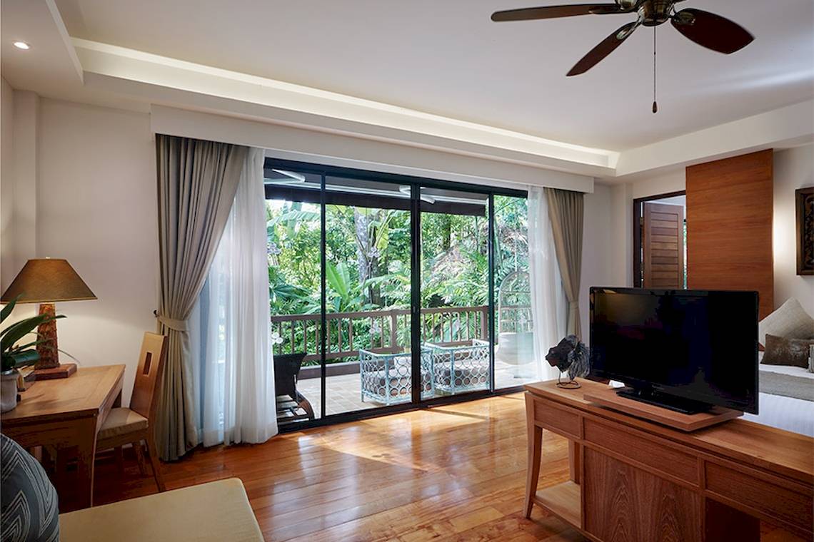 Innenansicht eines Zimmers im Khaolak Paradise Resort mit Fernseher, Tisch, Stühle und Balkon.
