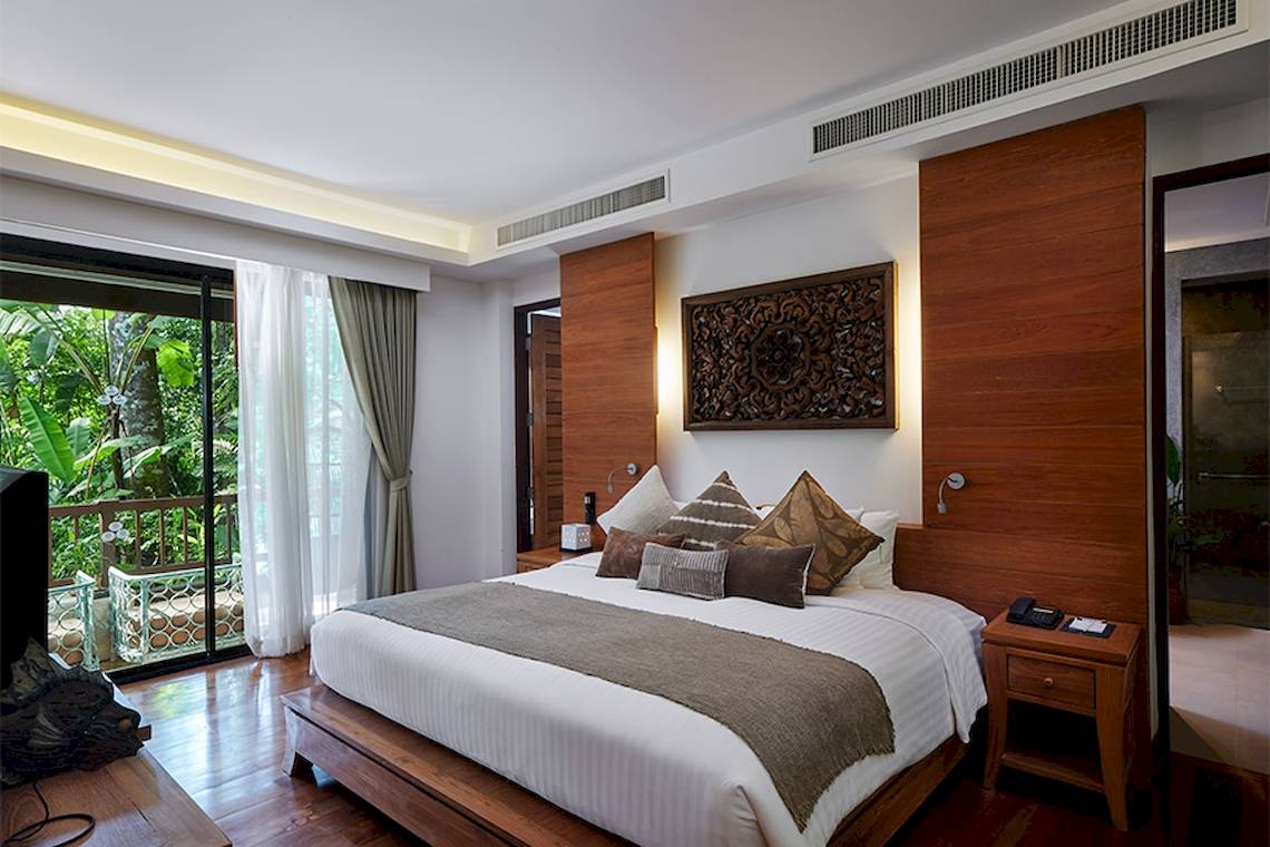 Khaolak Paradise Resort Zimmer mit Kingsize-Bett, Kissen, Decke und Ausblick auf Terrasse mit Bäumen