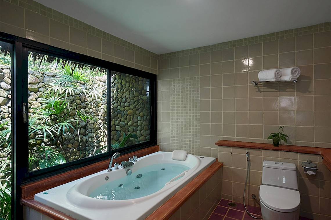 Ein Badezimmer mit einer Badewanne und einem Fenster, das einen Garten zeigt.
