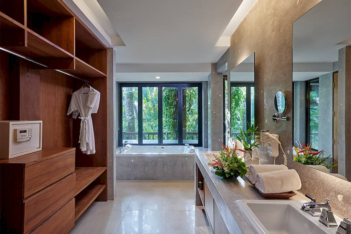 Badezimmer im Khaolak Paradise Resort mit Badewanne, Spiegel und Holzschrank.