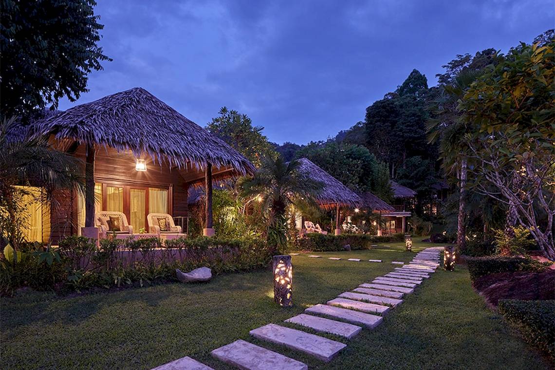 Außenansicht des Khaolak Paradise Resorts bei Nacht mit beleuchteten Hütten und einem gepflasterten Weg.