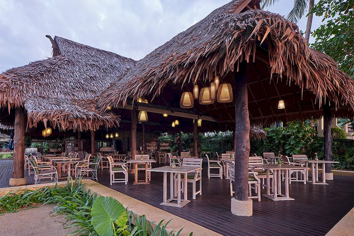 Außenbereich des Khaolak Paradise Resorts mit Tisch und Stühlen unter einem Strohdach.