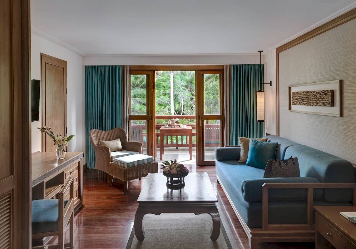 Wohnzimmer des Santiburi Koh Samui Hotels mit Blick auf eine Terrasse und Garten.