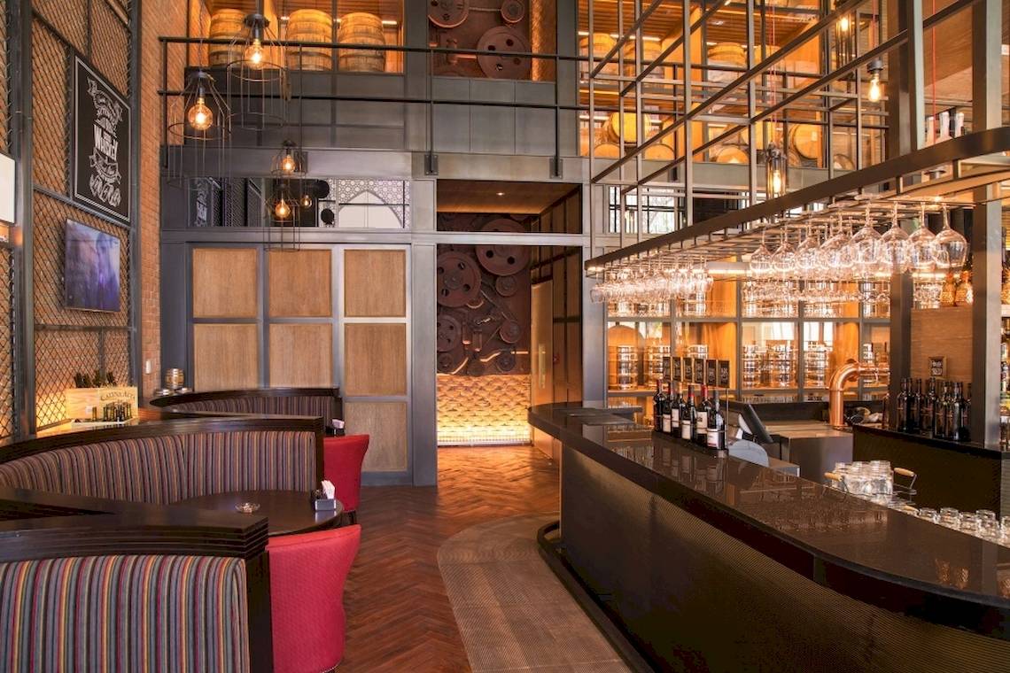 Innenansicht der Bar im Saadiyat Rotana Resort & Villas Hotel mit Sitzgelegenheiten und einer Theke voller Flaschen.