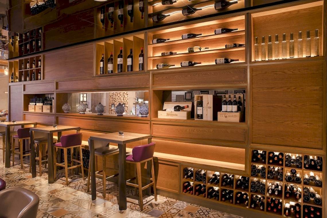 Ein Restaurantbereich im Saadiyat Rotana Resort & Villas mit Holztischen, Stühlen und Weinregalen an den Wänden.