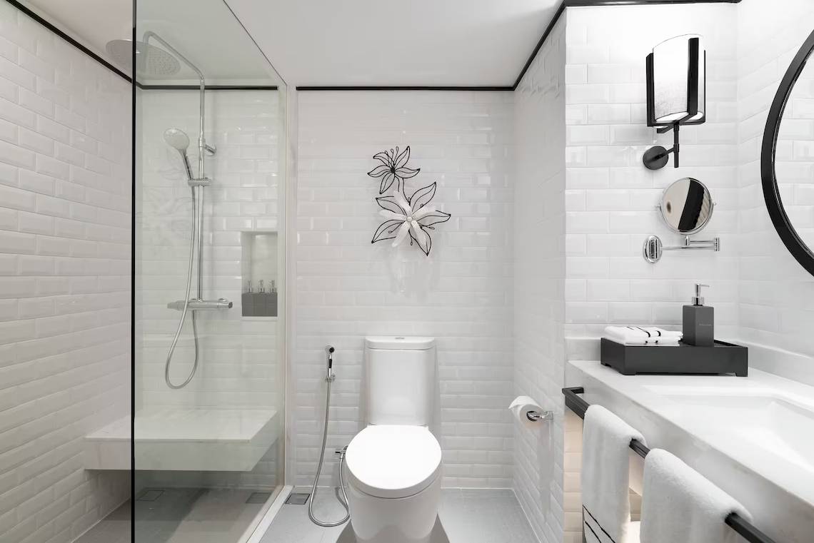 Modernes Badezimmer des Meliá Koh Samui Hotels mit weißen Fliesen und einer Glasdusche.