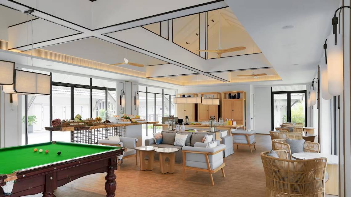 Loungebereich im Meliá Koh Samui mit grünem Pooltisch, weißen Möbeln und großen Fenstern.