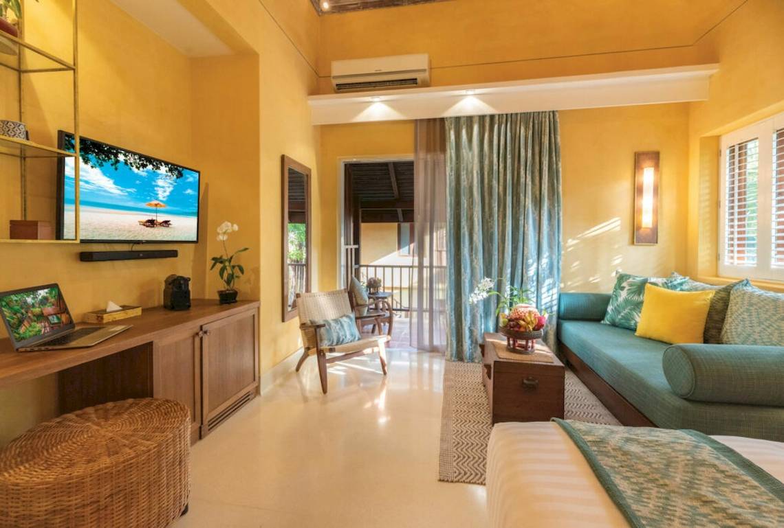 Wohnzimmer des Buri Rasa Village Samui Hotels mit Fernseher, Laptop, Couch und Bett.
