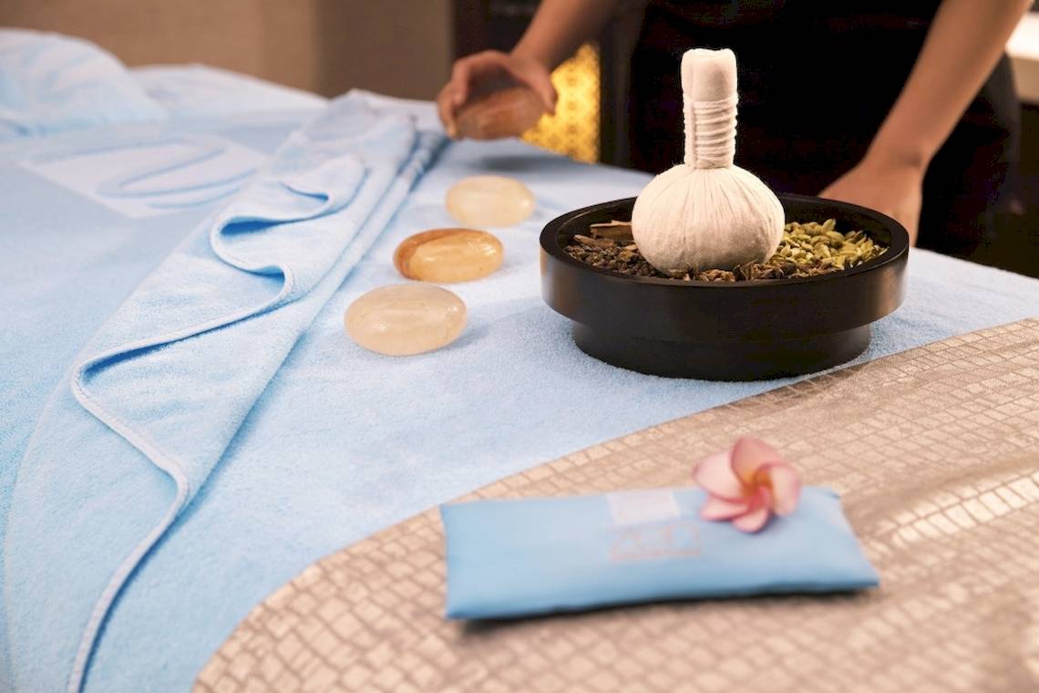 Massagetisch im Saadiyat Rotana Resort mit drei Steinen, einem Beutel und einer Blume.