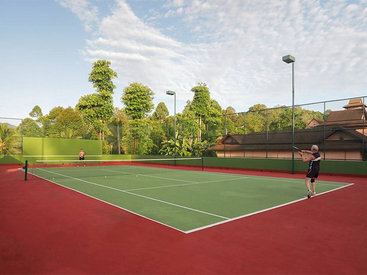 Tennisplatz im Freien im Khao Lak Merlin Resort mit zwei Spielern und umliegenden Bäumen.