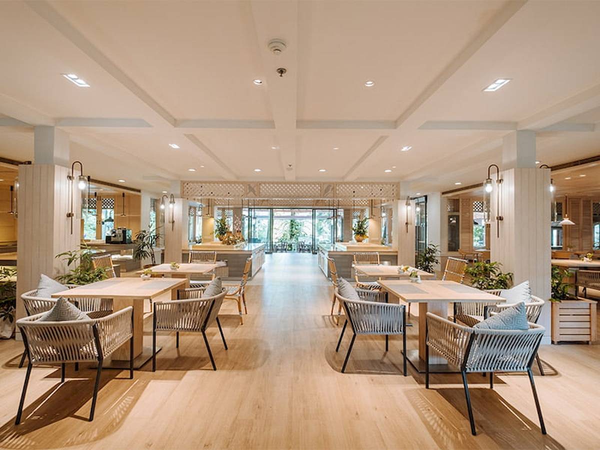 Innenbereich des Khao Lak Merlin Resorts mit hölzernen Tischen, Stühlen und Pflanzen.