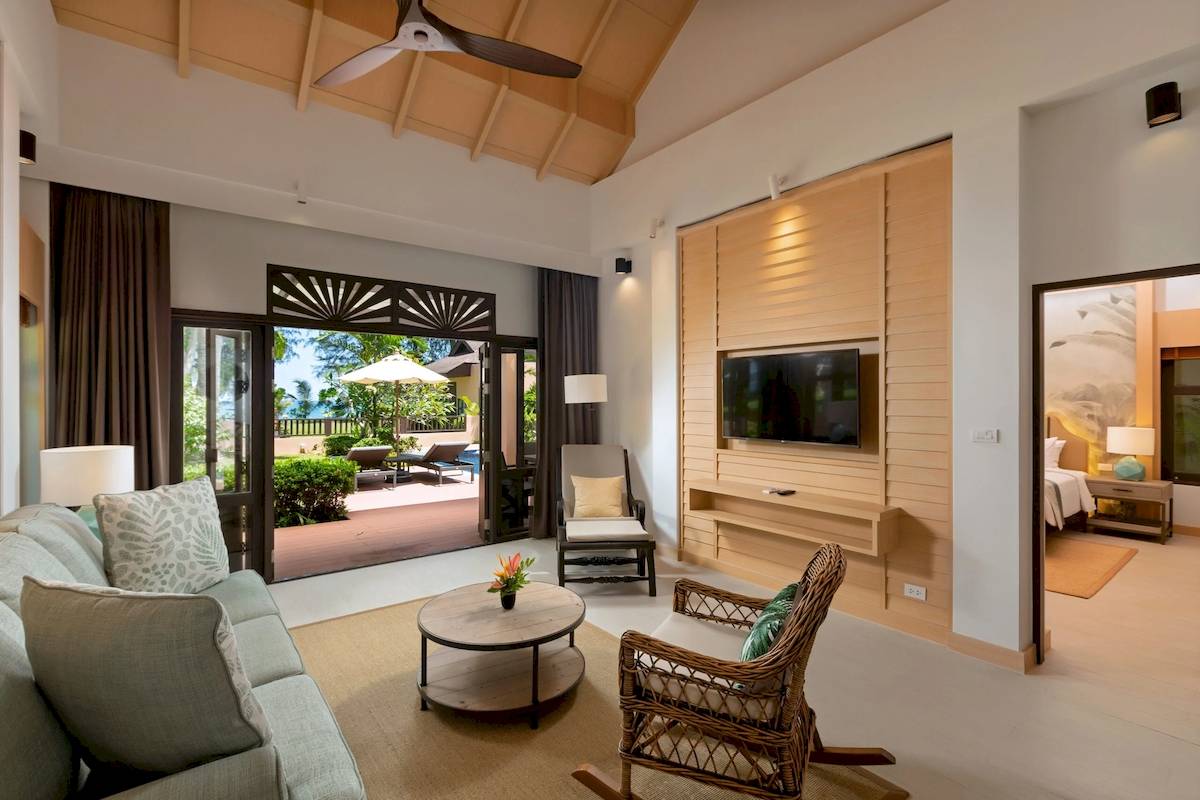 Wohnzimmer des Khao Lak Merlin Resorts mit Sofa, Tisch, Stuhl und Fernseher.