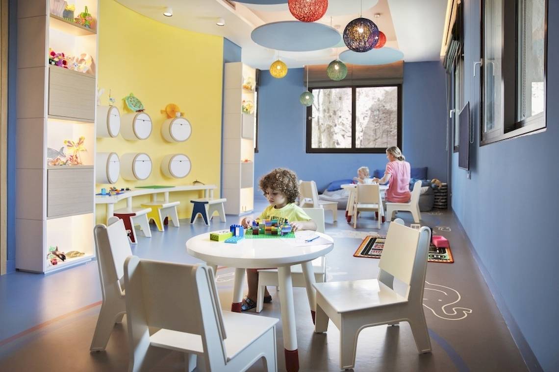 Ein farbenfrohes Kinderzimmer im Saadiyat Rotana Resort mit einem Kind, das Legos auf einem Tisch baut.