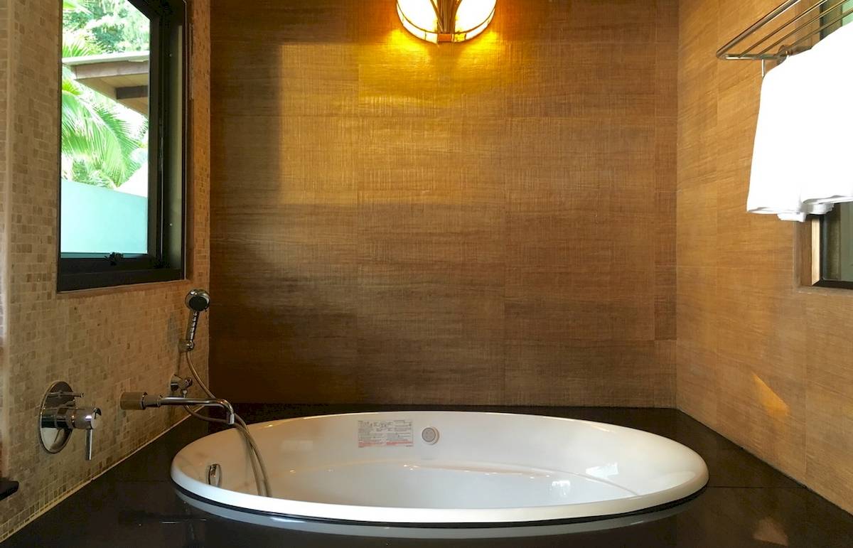 Badezimmer des Tup Kaek Sunset Beach Resorts mit einer Badewanne, einer Wand aus Holzimitat und einem Fenster.
