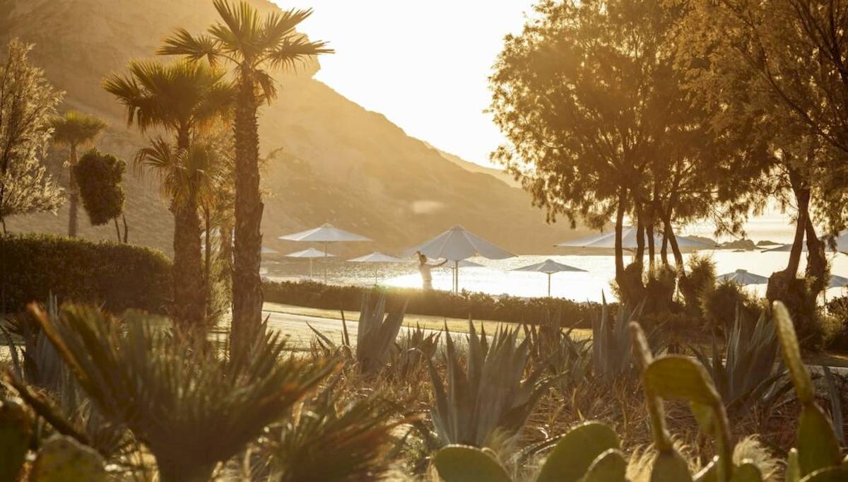 Sonnenaufgang im Ikos Aria Hotel mit vielen weißen Sonnenschirmen und einem Berg im Hintergrund.