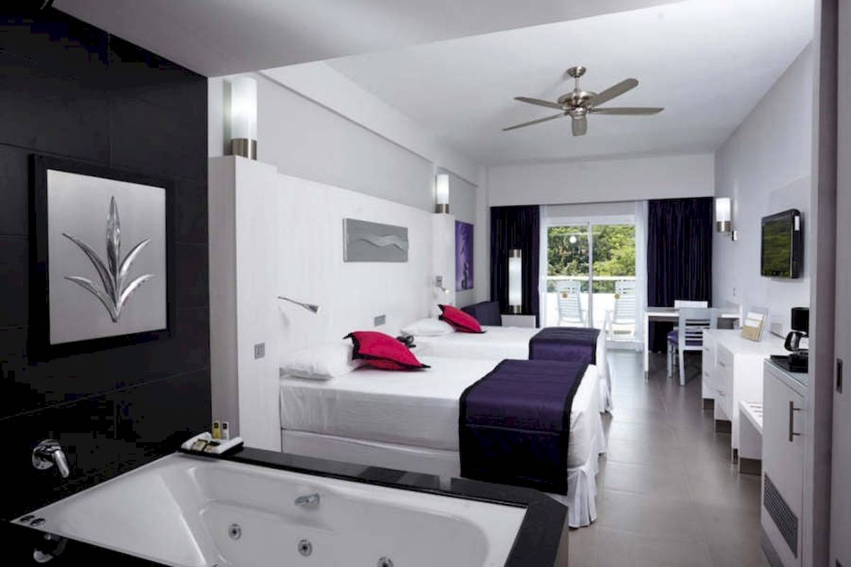 Innenansicht der Suite im Riu Palace Costa Rica mit zwei Betten, Badewanne und modernen Möbeln.