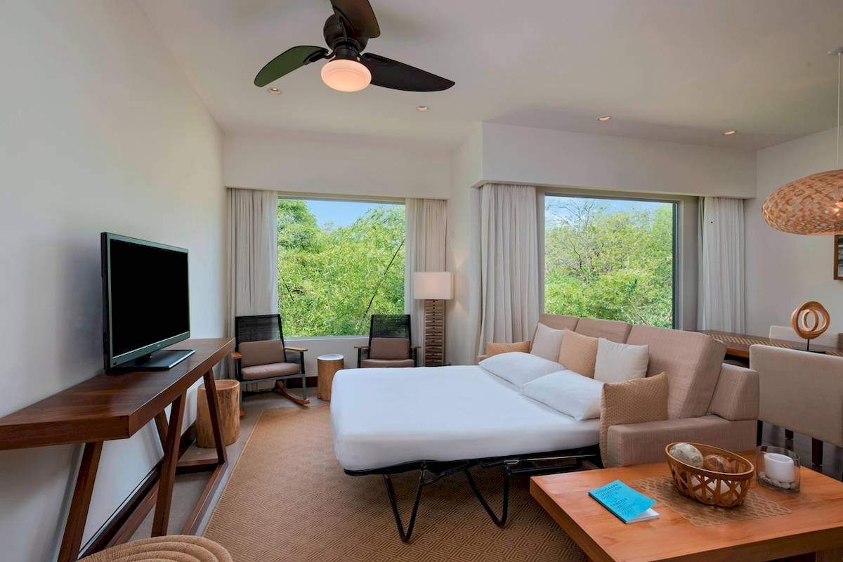 Wohnzimmer im El Mangroove, Autograph Collection Hotel mit Fernseher, Sofa, Tischen und Stühlen.