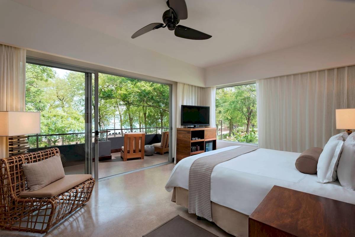 Hotelzimmer mit Balkon, Ausblick auf Wald und Wasser, modernes Design.