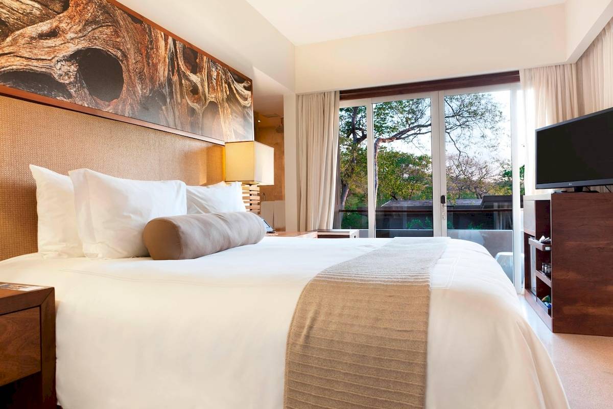 Schlafzimmer im El Mangroove, Autograph Collection Hotel mit großem Bett, Fenstern und Fernseher.
