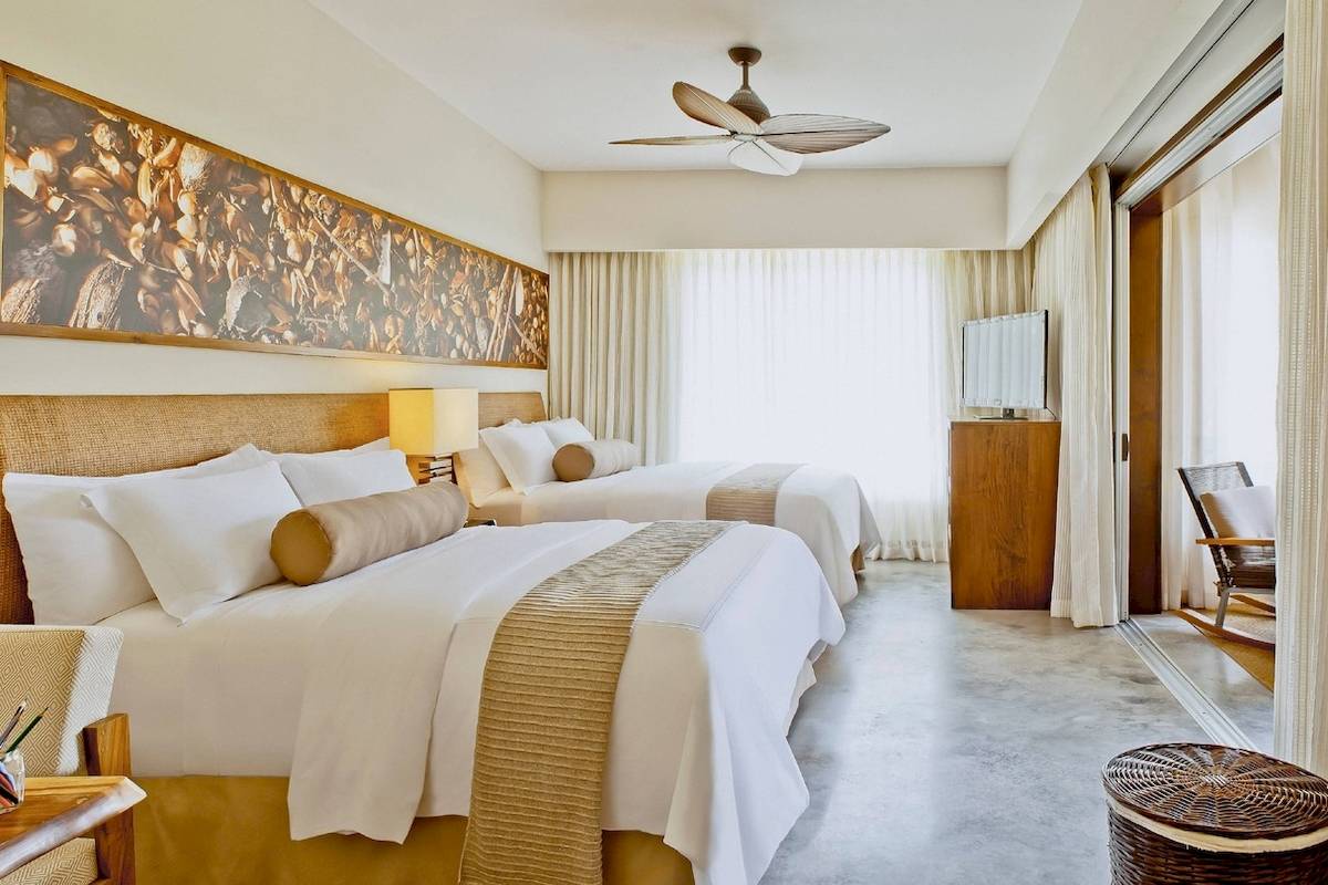 Zwei Betten in einem eleganten Hotelzimmer des El Mangroove, Autograph Collection, mit einem großen Wandbild und modernen Möbeln.
