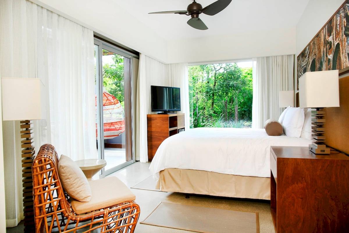 Innenansicht des Hotelzimmers El Mangroove, Autograph Collection mit Bett, Fernseher und Aussicht auf Bäume.