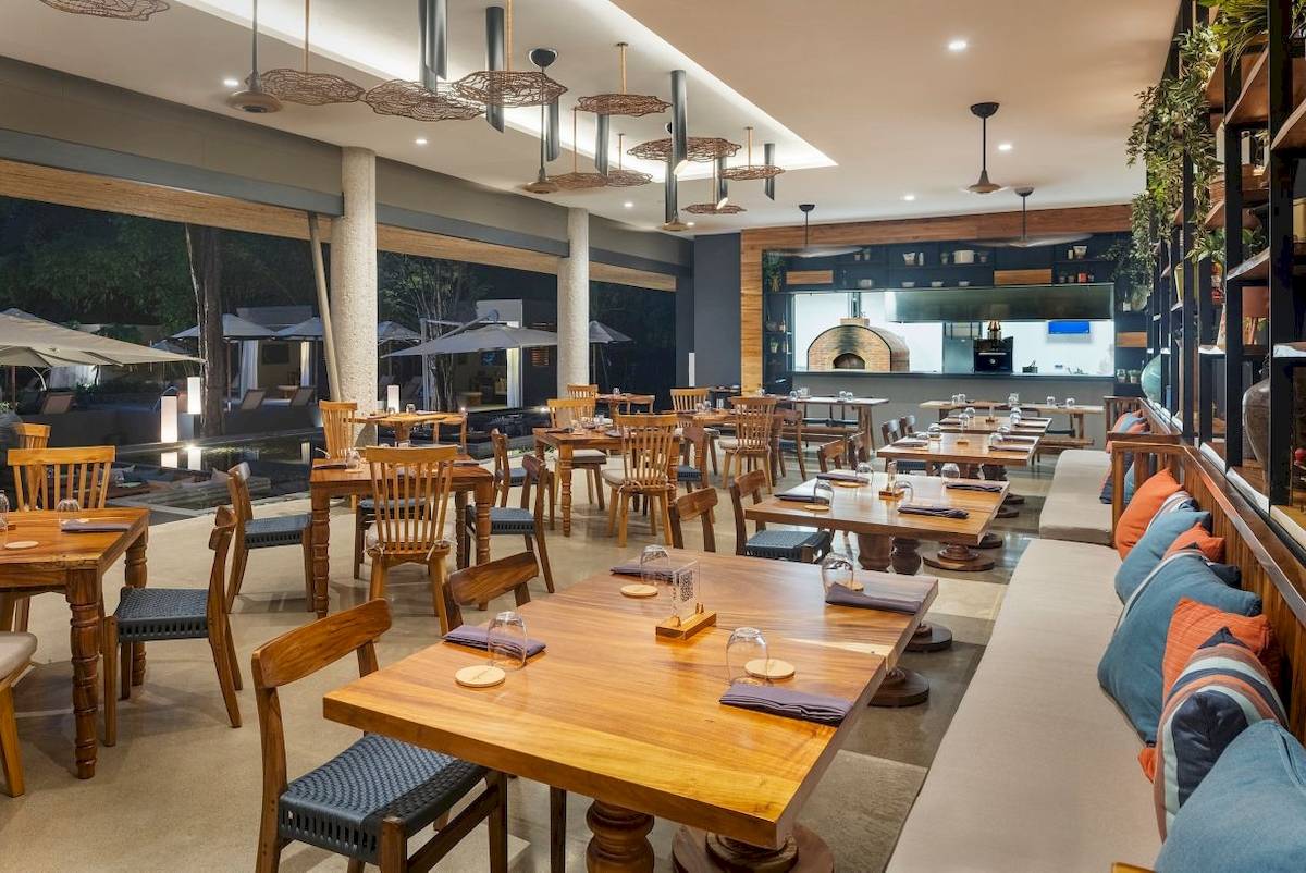 Innenansicht des Restaurants im El Mangroove, Autograph Collection mit Holztischen, Stühlen und einer Bar.