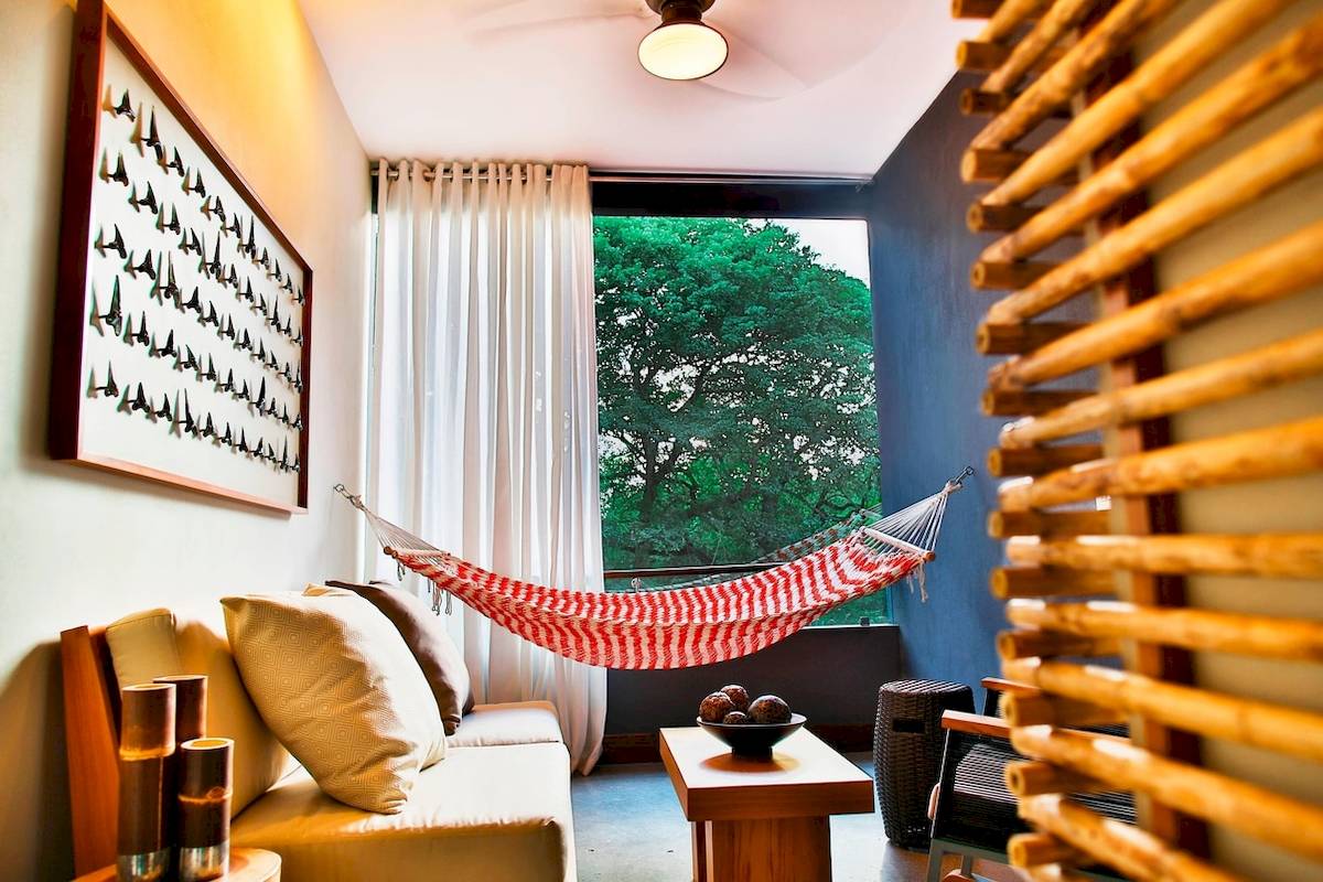 Wohnzimmer eines Hotels mit einem roten und weißen Hängematten über einem Sofa und einem Ausblick auf einen Baum.