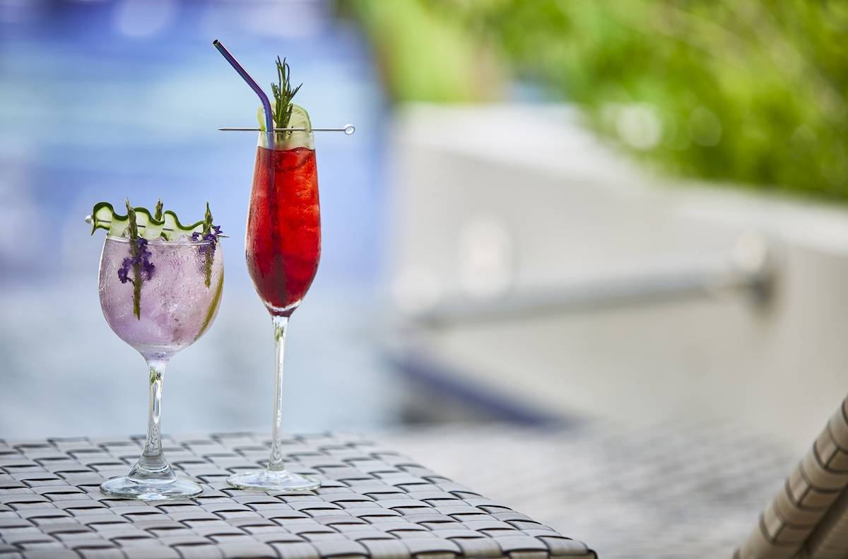 Zwei Cocktails mit lavendelfarbenem Getränk und grünen Dekorationen auf einem Tisch am Pool.