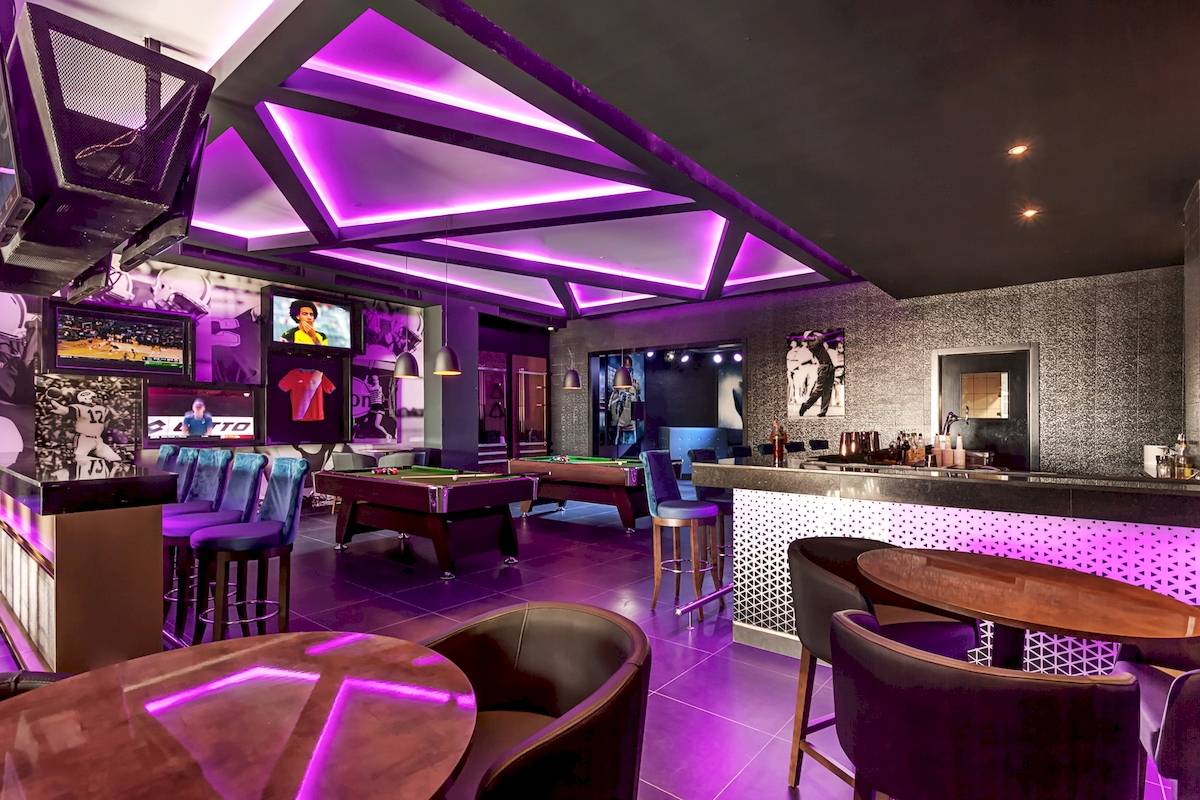 Innenansicht der Poolbar im Planet Hollywood Beach Resort mit violetten Beleuchtung, Billardtischen und Bar.