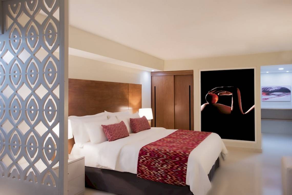 Schlafzimmer im Emotions By Hodelpa Puerto Plata Hotel mit Bett, Kissen, Nachttisch und Wandkunst.