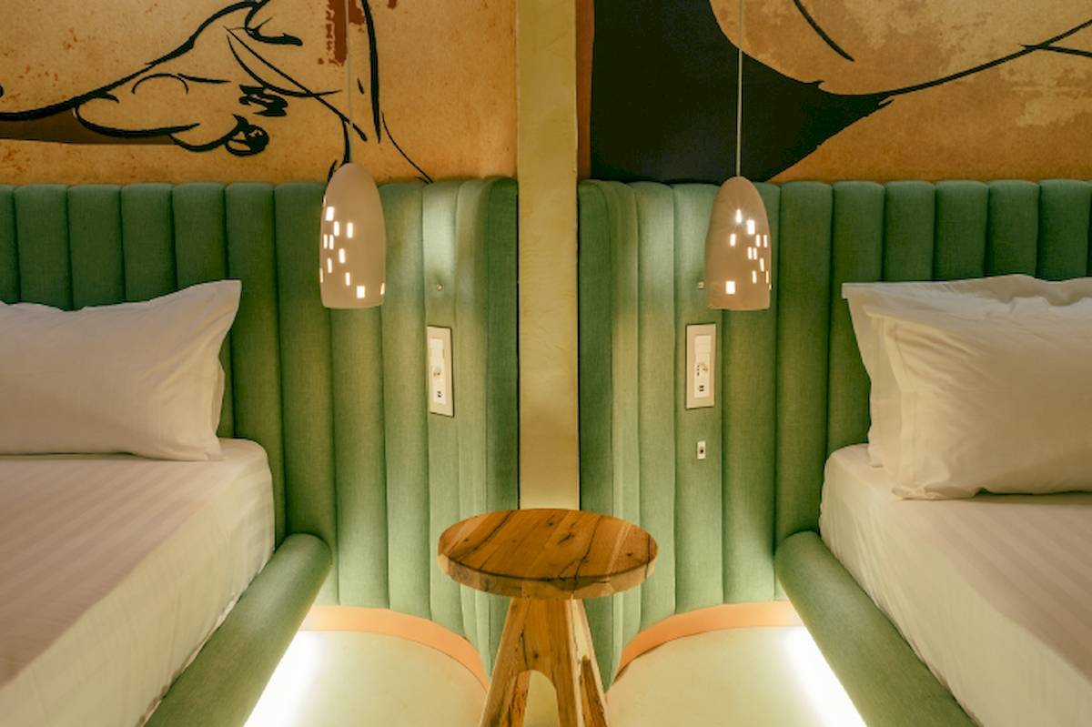Doppelbettzimmer im Epidamn White Sensation Hotel mit grünen Kopfteilen, weißen Laken und Kissen, und einem kleinen Holztisch dazwischen.