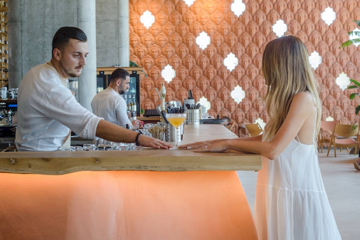 Barkeeper serviert eine Frau im weißen Kleid ein Getränk im Epidamn White Sensation Hotel.