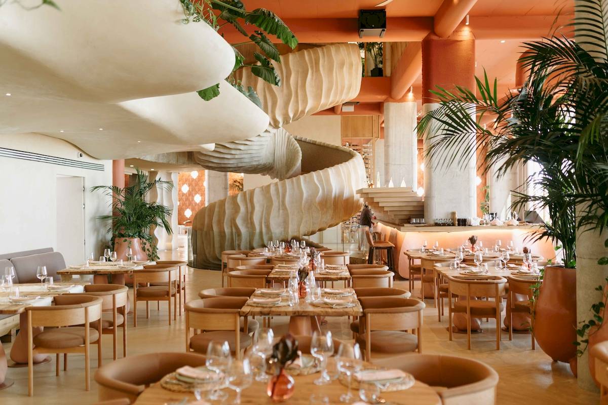 Innenbereich des Epidamn White Sensation Hotels mit einem großen spiralförmigen Treppenaufgang und runden Tischen.