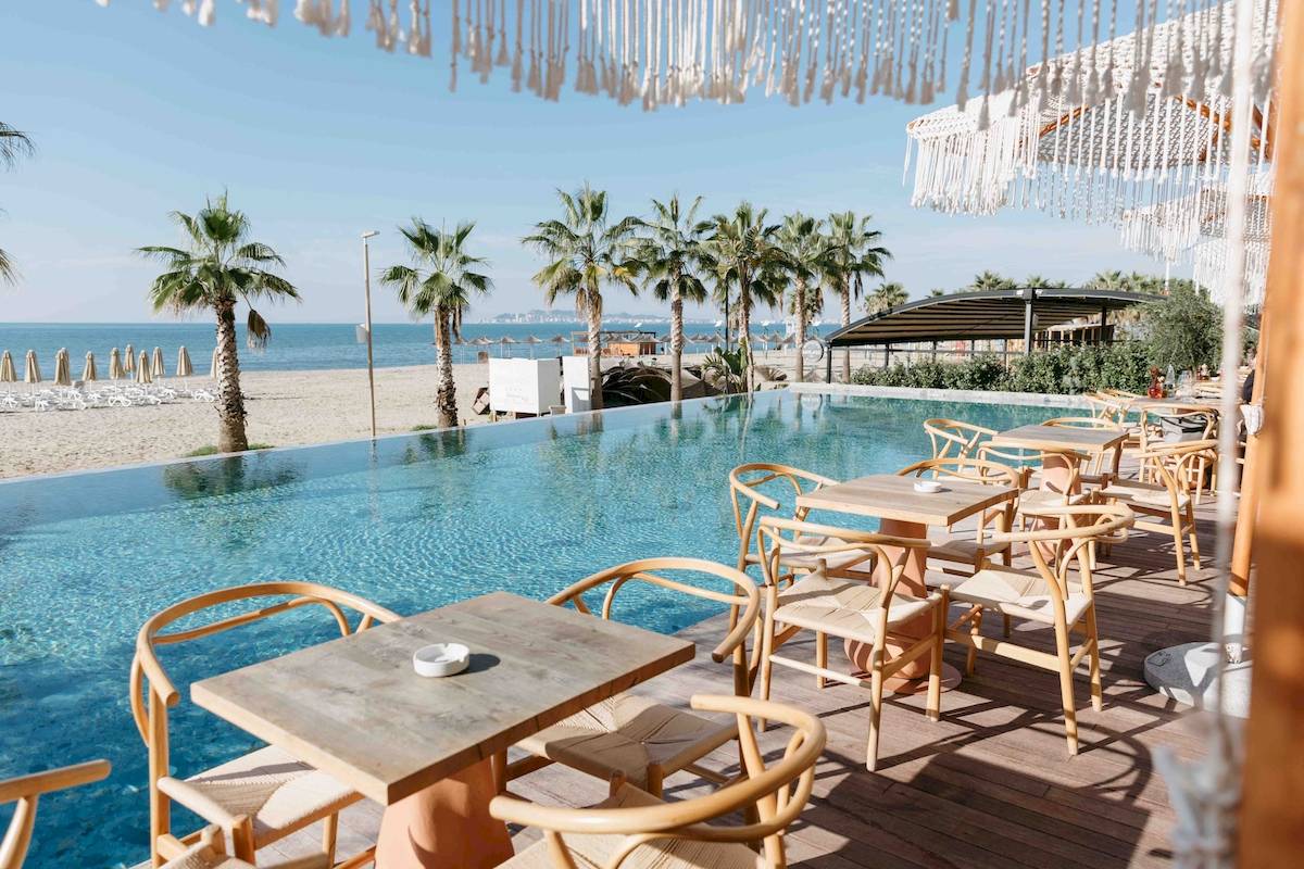 Außenterrasse des Epidamn White Sensation Hotels mit Tischen und Stühlen neben einem Pool und Blick auf den Strand
