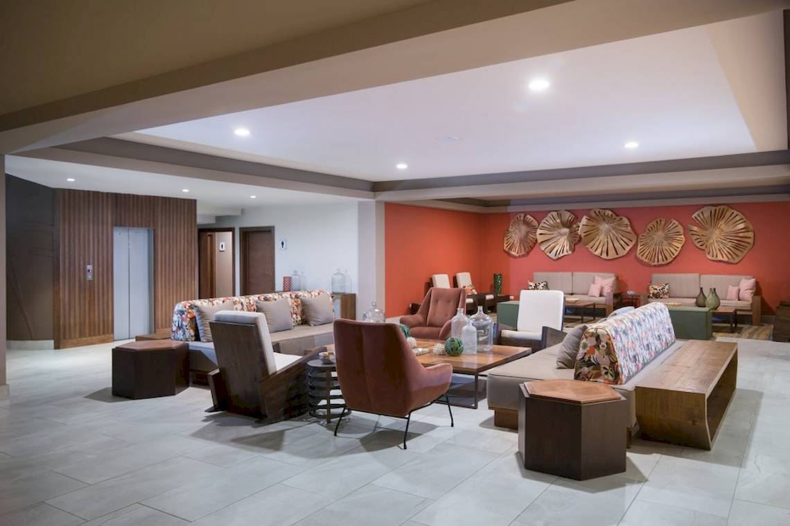 Lobby des Emotions By Hodelpa Puerto Plata mit Sofas, Tischen und Wanddekorationen.