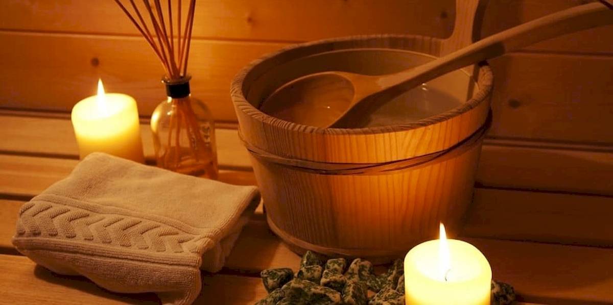 Eine Sauna mit einer Holzbadewanne, einem Holzlöffel, zwei Kerzen und einem Handtuch.