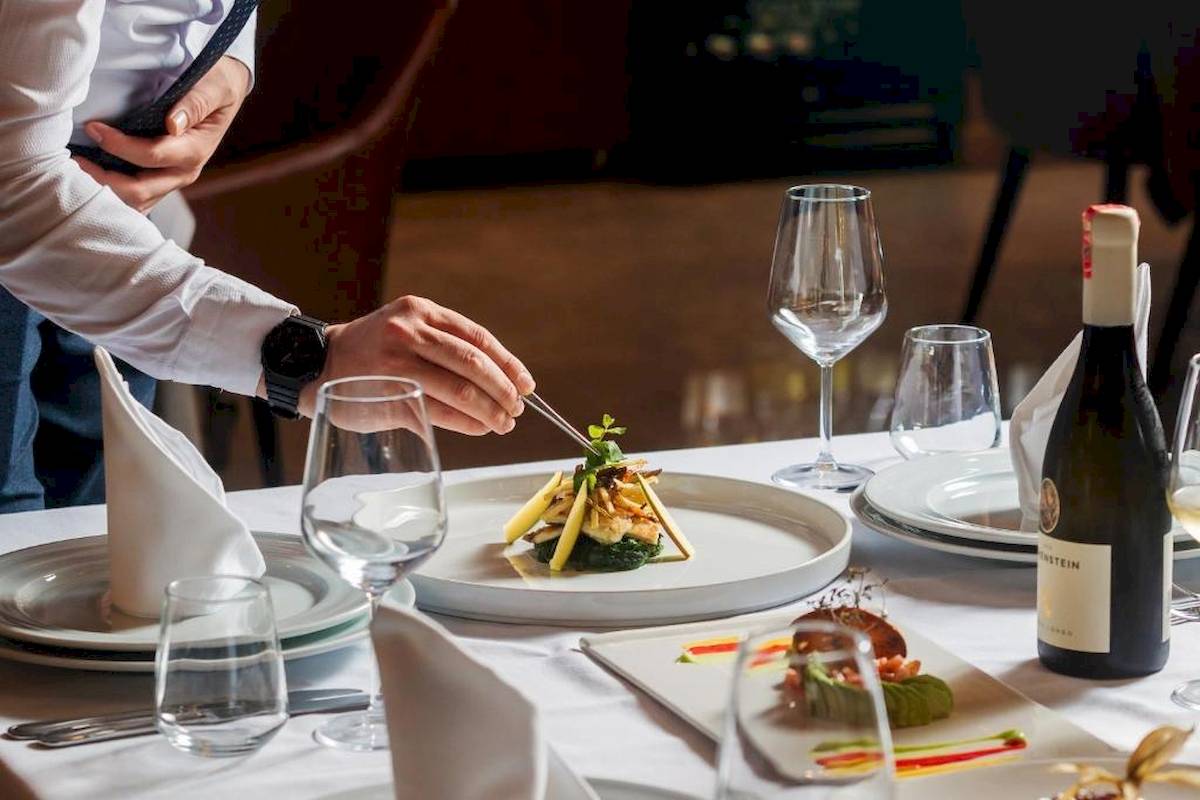 Elegantes Tischsetting im Restaurant des Gloria Palace Hotel & SPA mit Gerichten und Weinflasche.