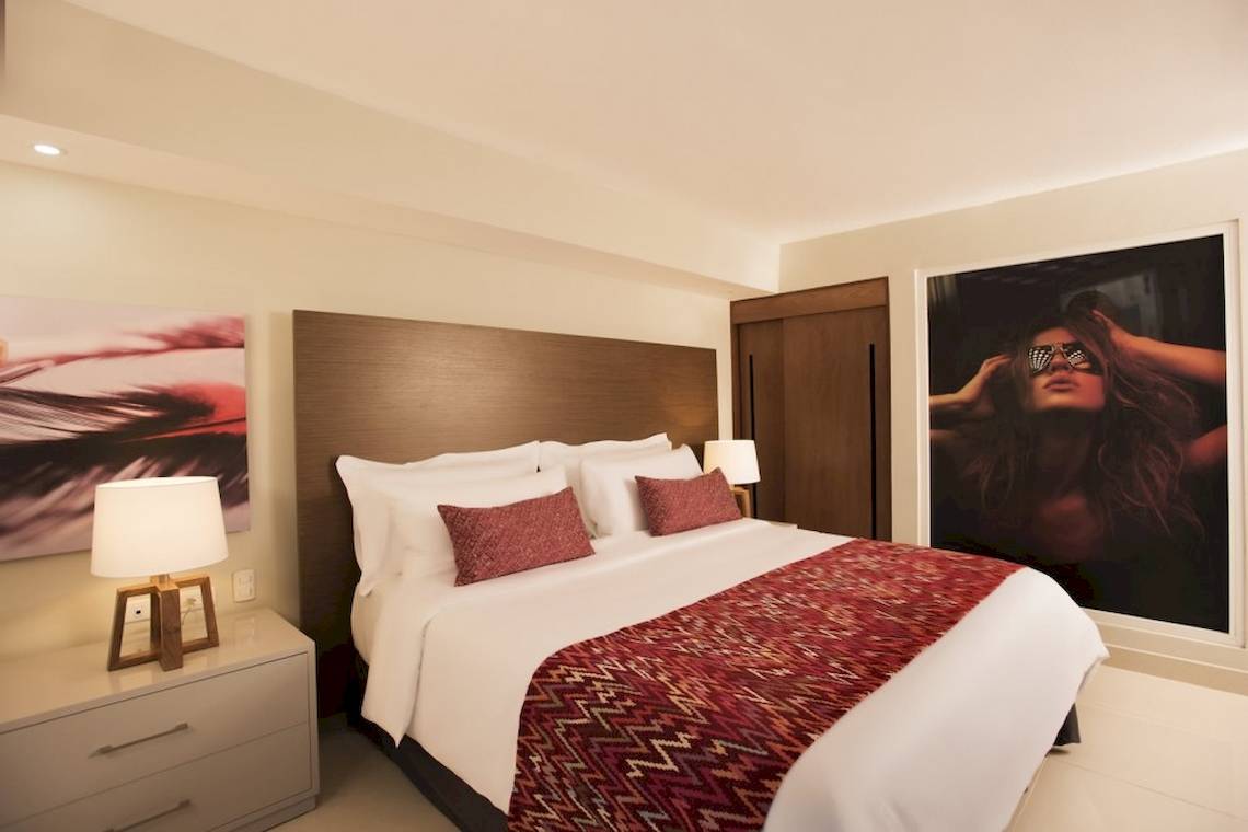 Schlafzimmer im Emotions By Hodelpa Hotel in Puerto Plata mit einem großen Bett, Kunstwerken an der Wand und Nachttischen.