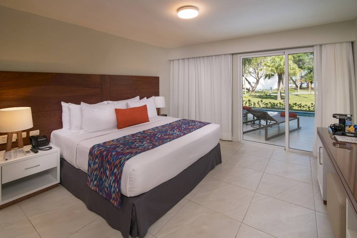 Hotelzimmer im Emotions By Hodelpa Puerto Plata mit Doppelbett, Poolblick und Glastür.
