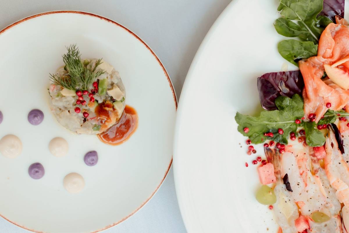 Zwei Teller mit Gerichten vom Klajdi Resort & SPA auf weißem Hintergrund.