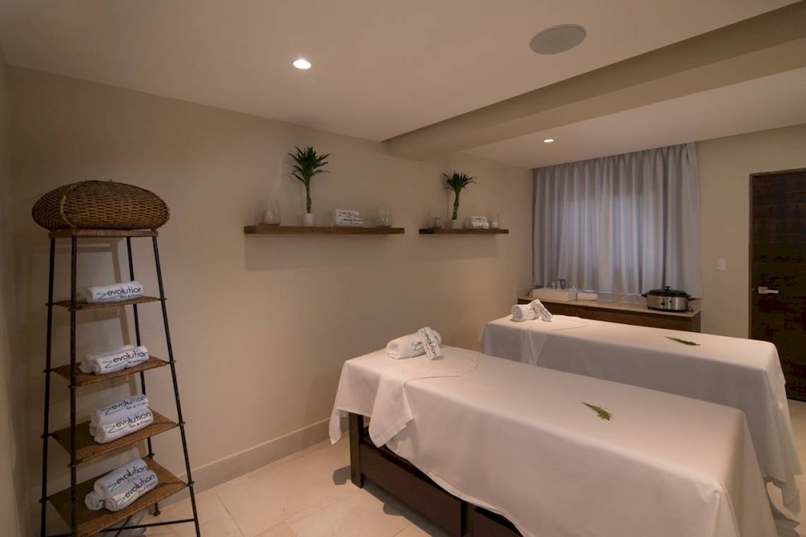 Massageraum im Emotions By Hodelpa Hotel mit zwei Massagetischen und einer Holzregal.