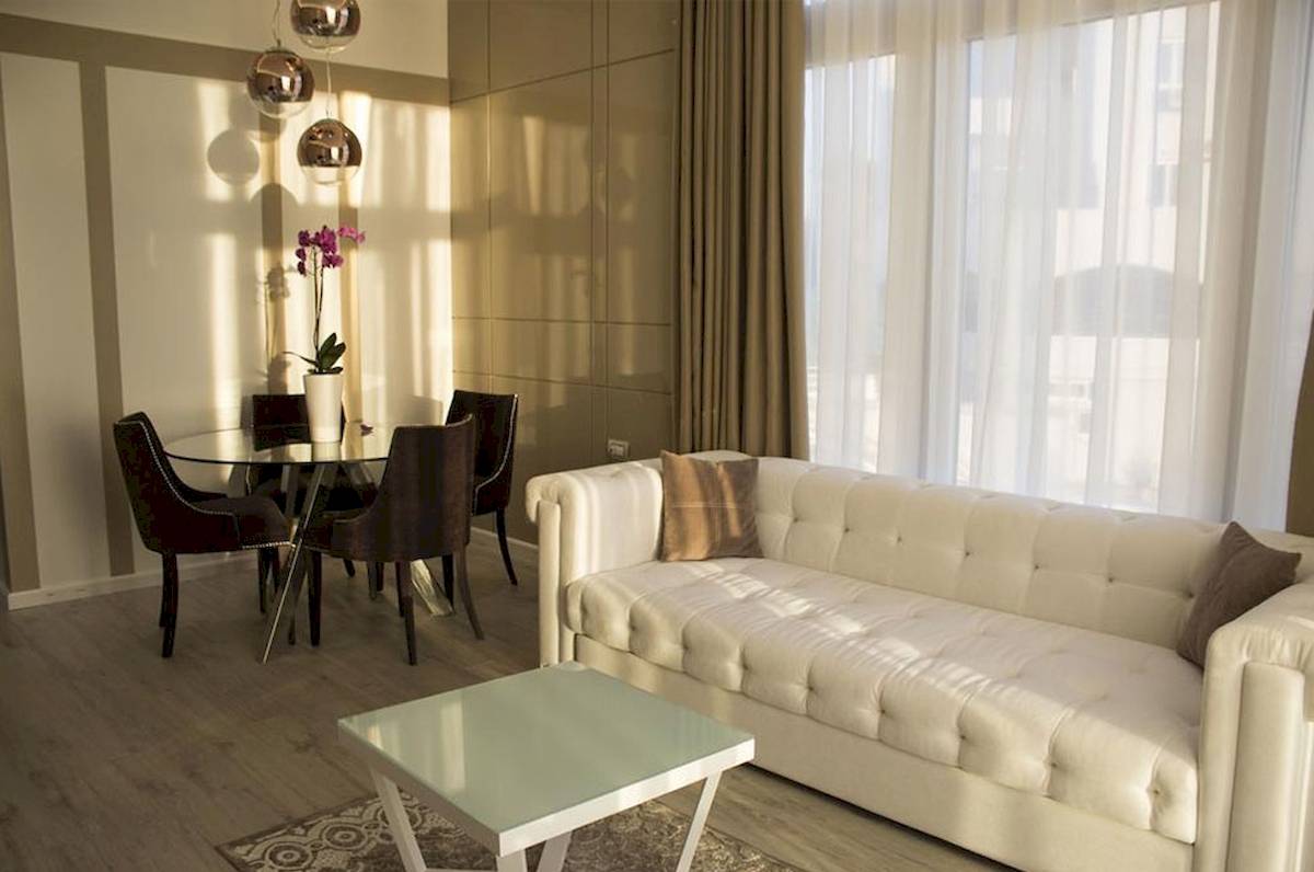 Wohnbereich im Demi Hotel mit weißem Sofa, Glastisch und Esstisch mit Blumenvase