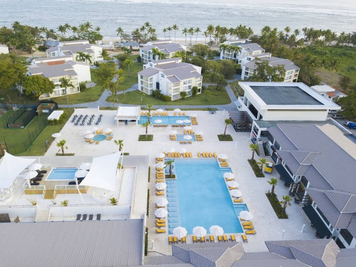 Außenansicht des Emotions By Hodelpa Puerto Plata Resorts mit Swimmingpools, Sonnenliegen und Gebäuden am Meer.