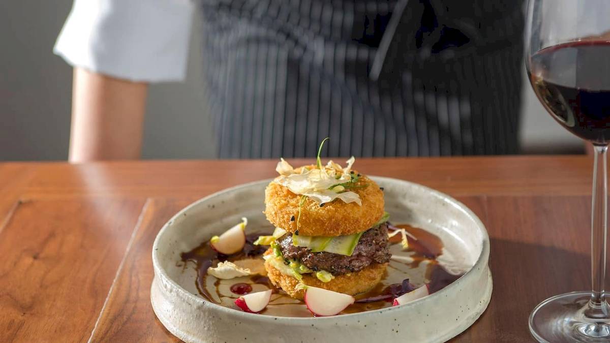 Ein Burger in einer Schale mit Rotkohlscheiben und Sauce auf einem Holztisch.