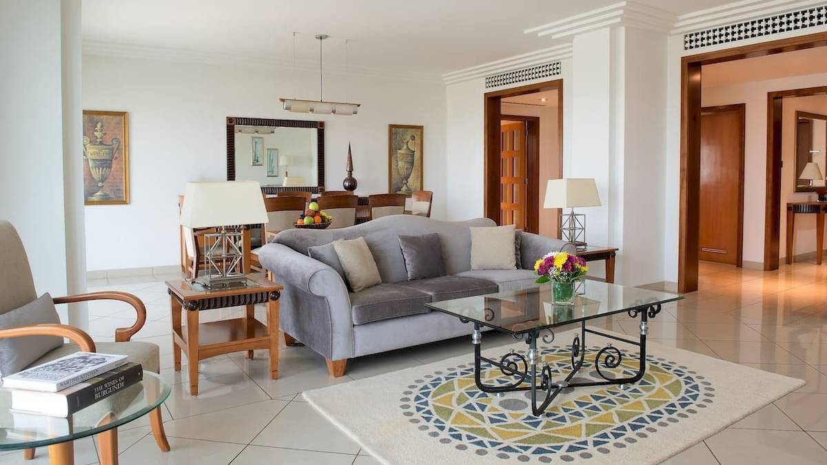 Wohnzimmer des Grand Hyatt Dubai mit grauem Sofa, Glastisch, Blumenvase und zwei Lampen.